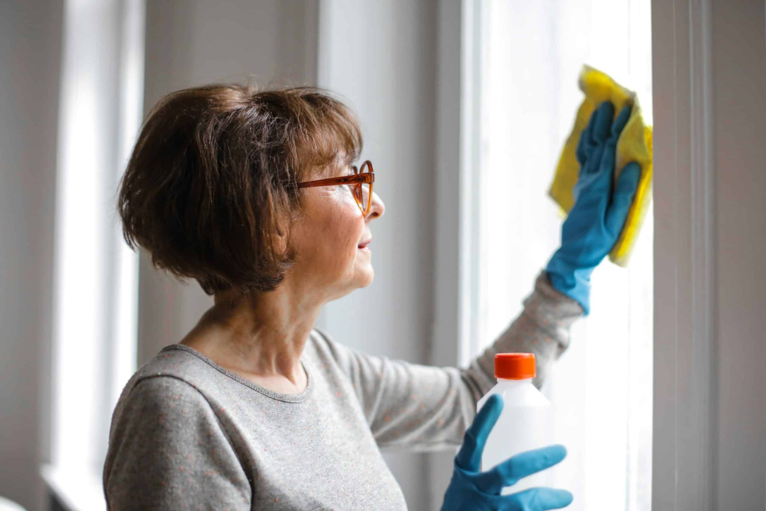 Older woman wiping down a window.