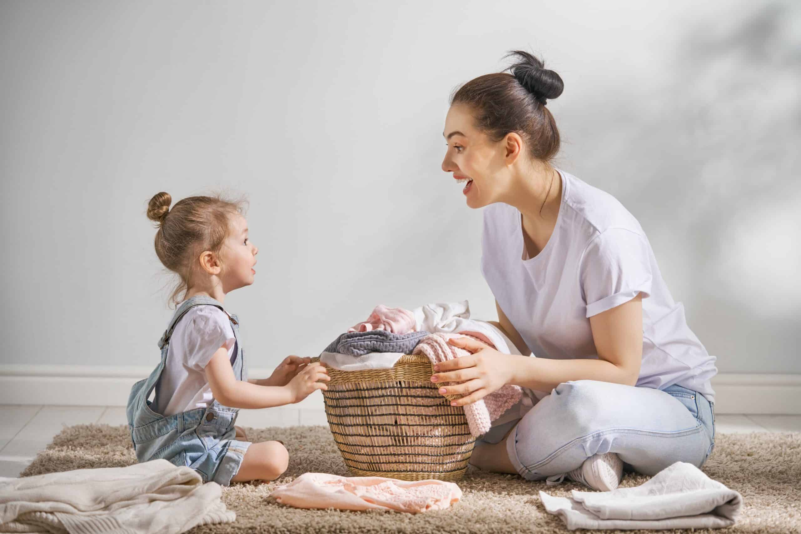 Young mother and toddler daughter around a laundry basket.