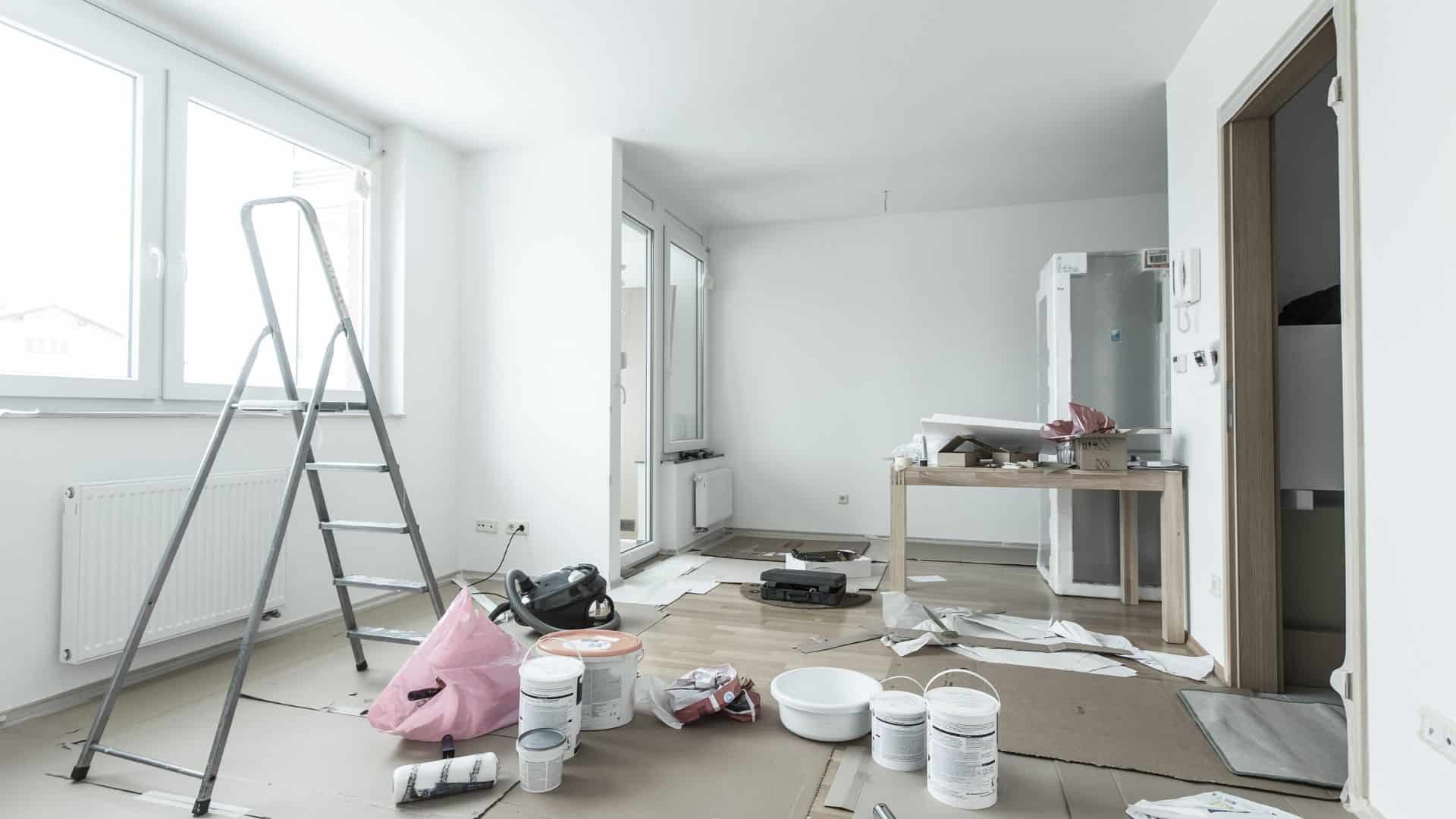 Vacant home with paint, ladder, and supplies on the floor covered with cardboards.