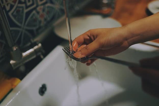 Woman washing a fork at a sink.