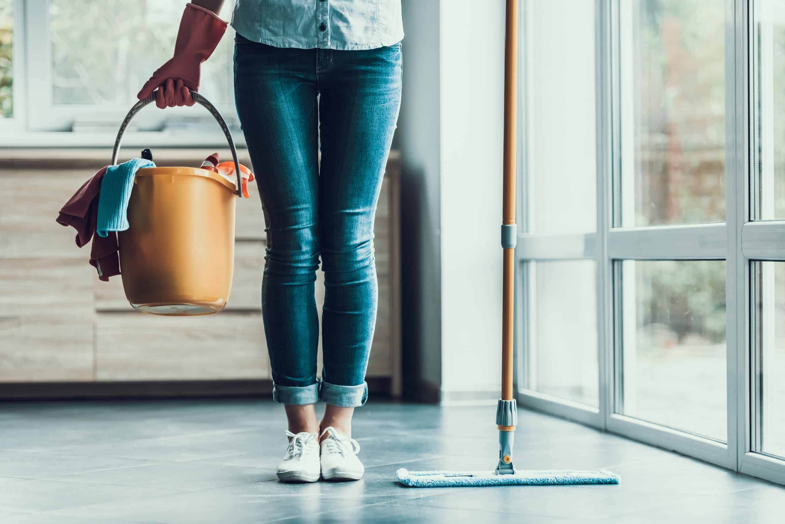 Closeup of woman wearing gloves holding bucket with cleaning supplies ready to start cleaning.