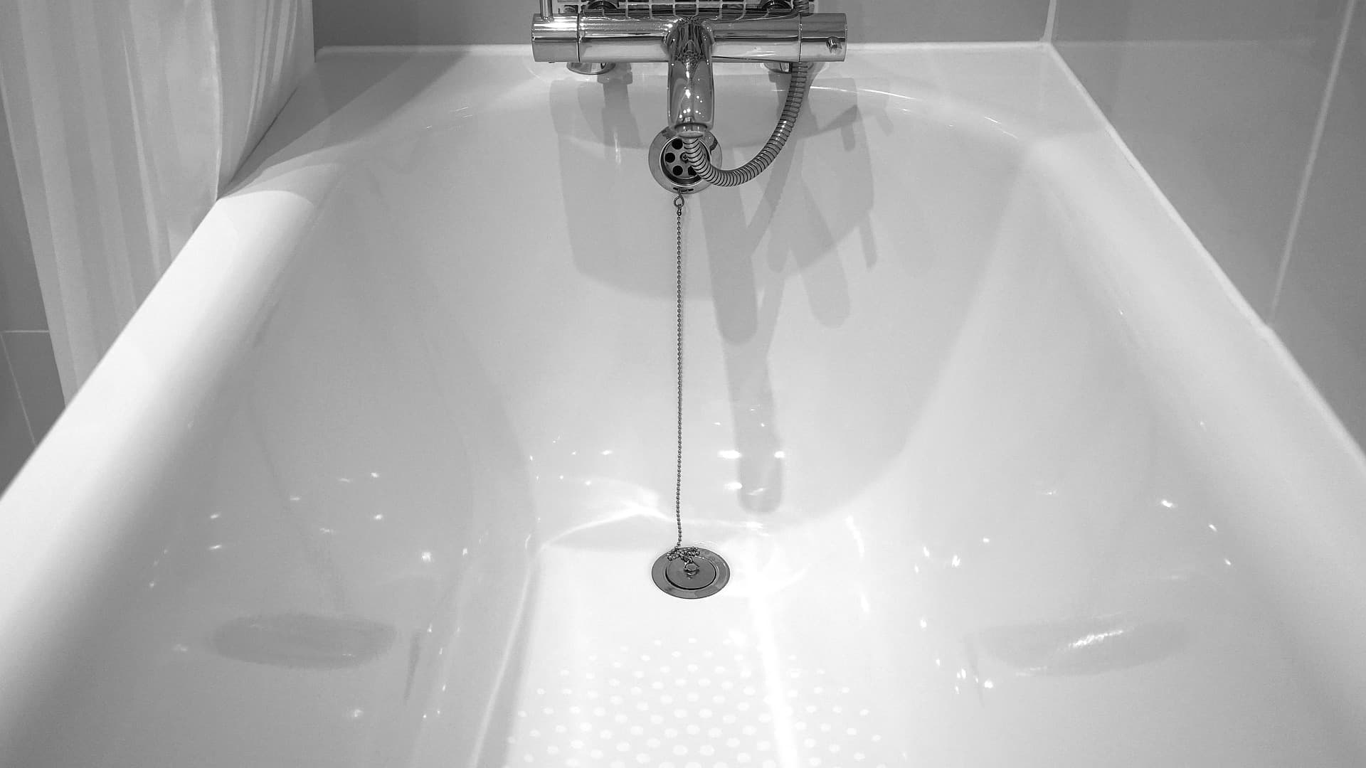 Bathtub against gray tile with white caulk.