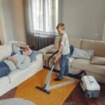 Boy cleaning rug with sick father on couch.