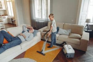 Boy cleaning rug with sick father on couch.