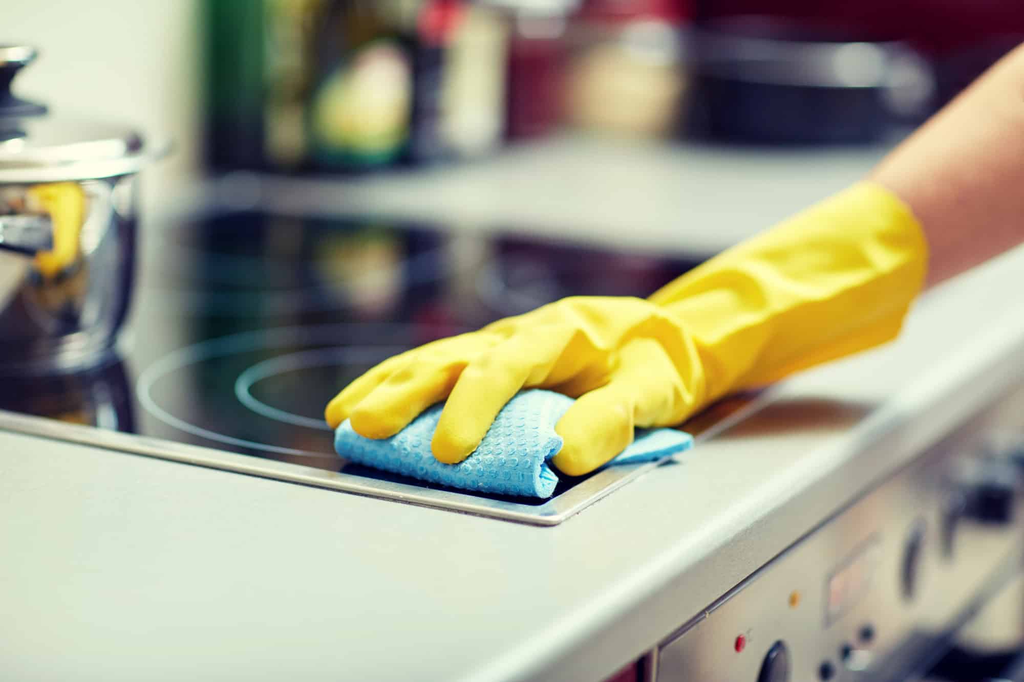 Close up of woman cleaning stove top at home kitchen.