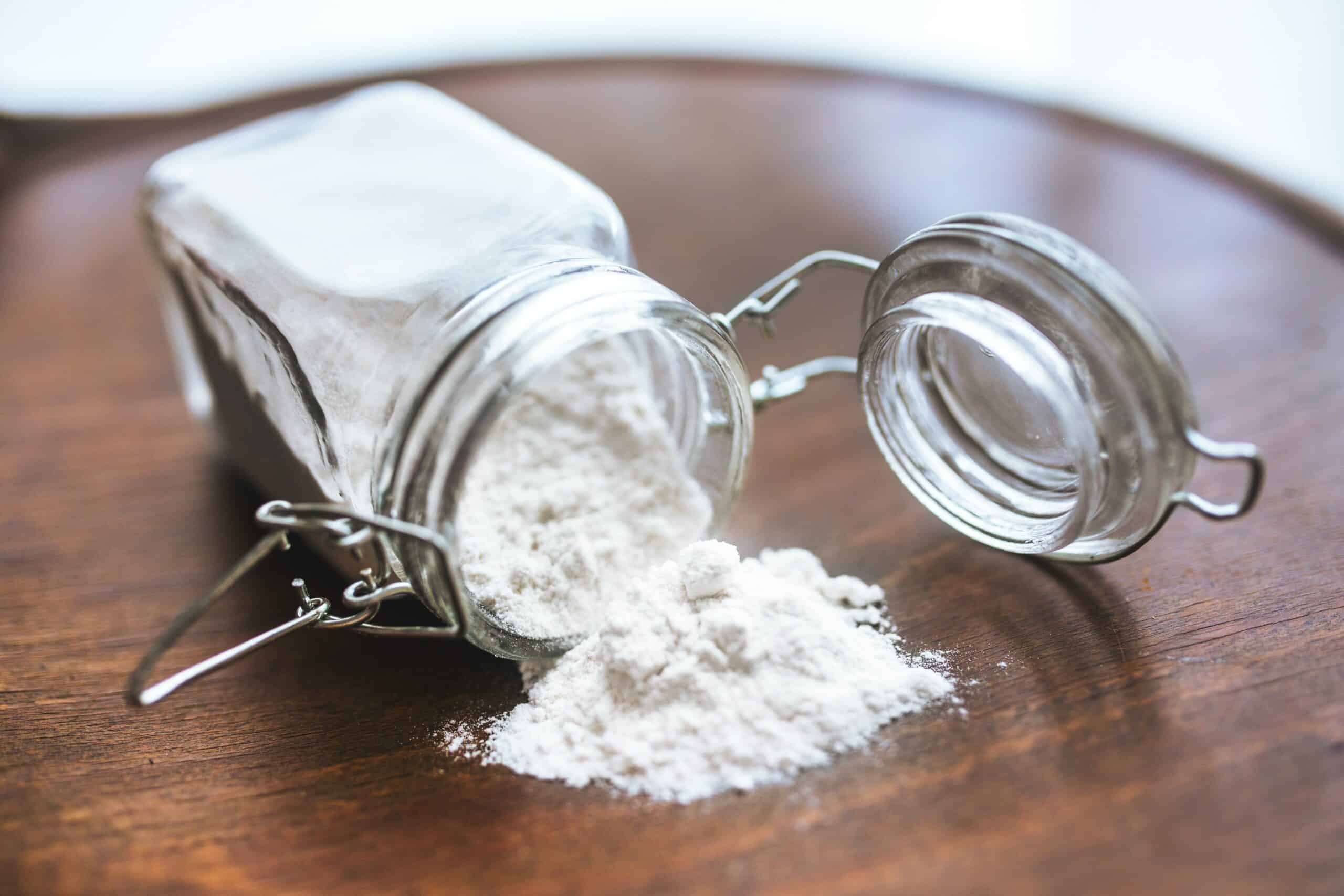 Glass jar spilling baking soda on table.