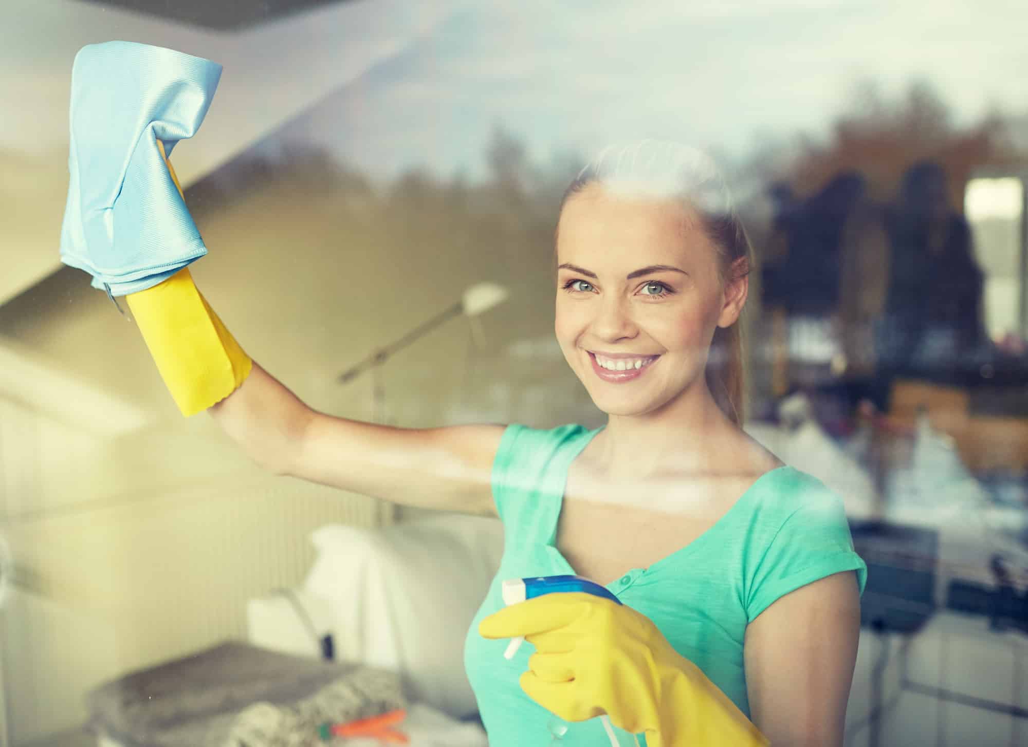 Happy woman in gloves cleaning window with cleaning cloth.