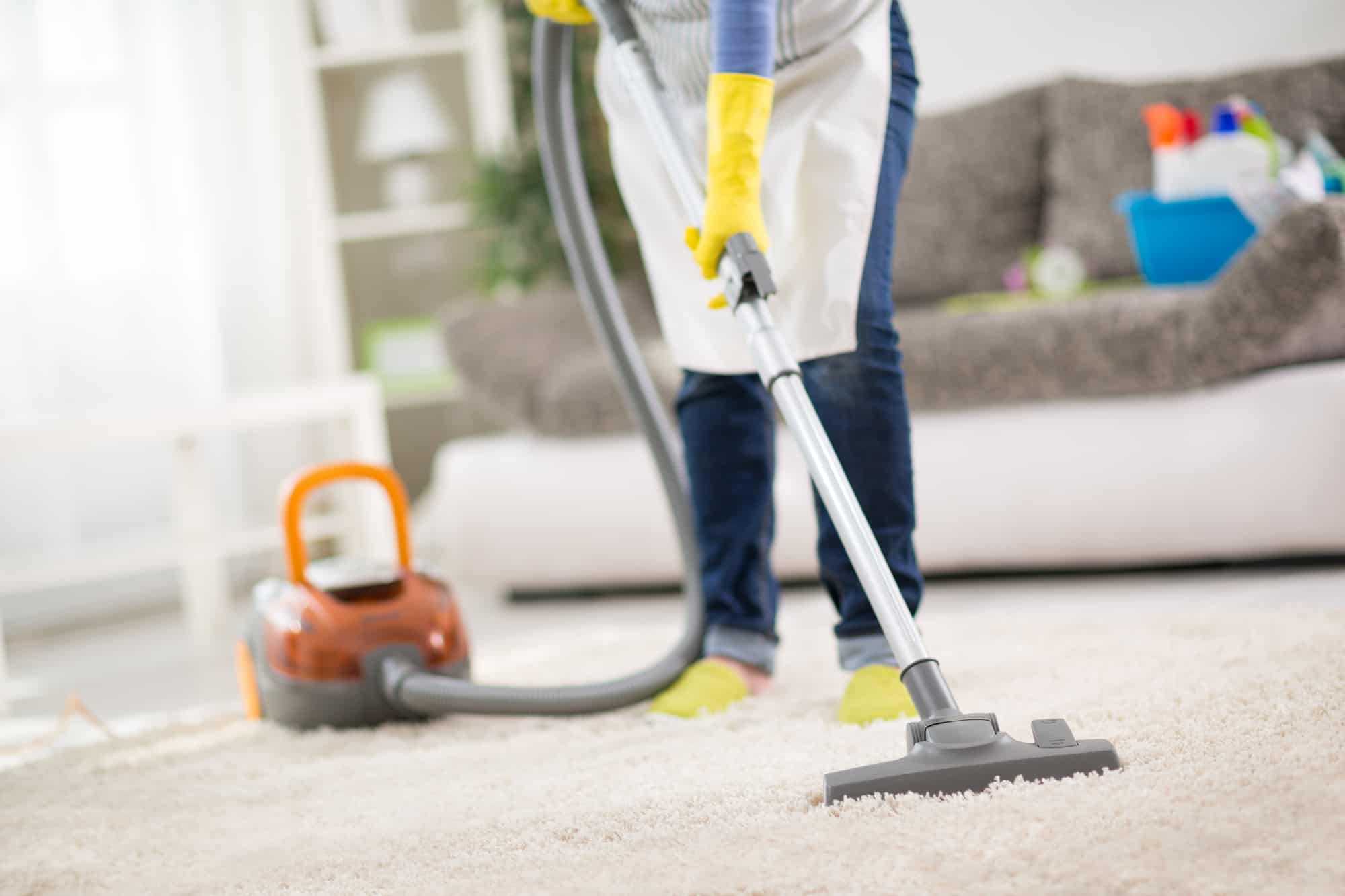 Woman with an apron on vaccuming a carpet at home.