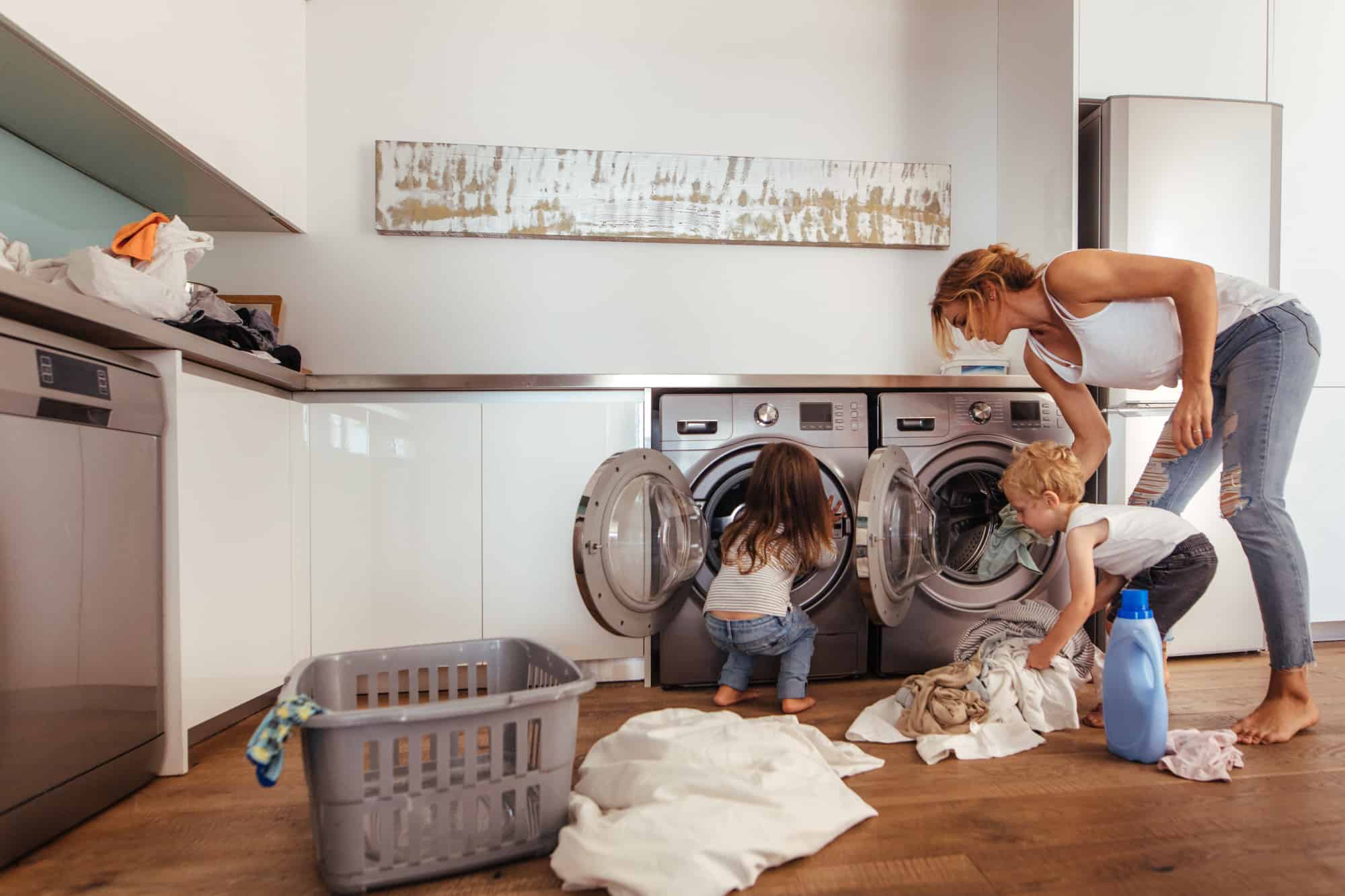 Woman with kids loading clothes in washing machine.
