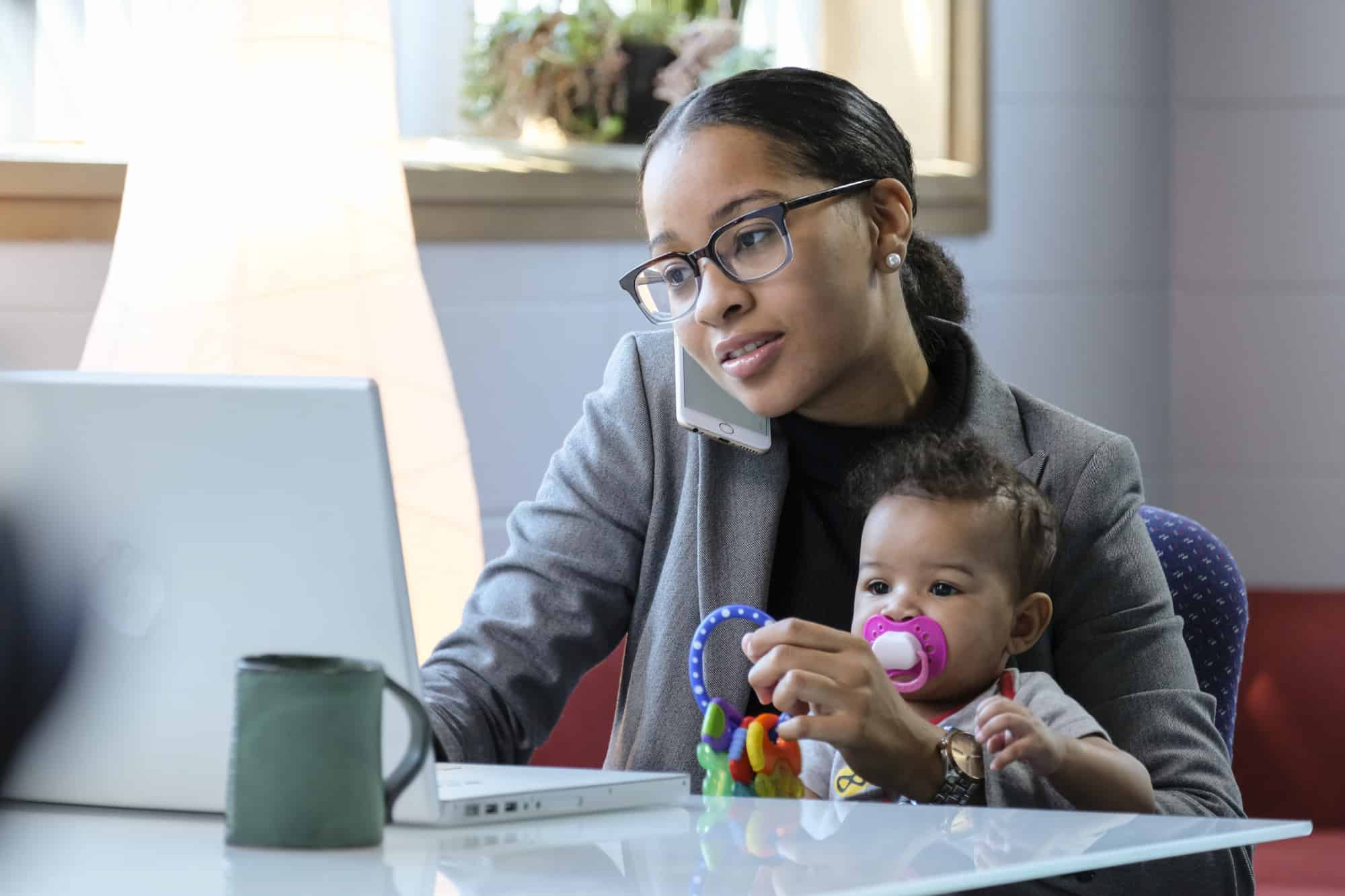 Mother holding baby and working at her computer.