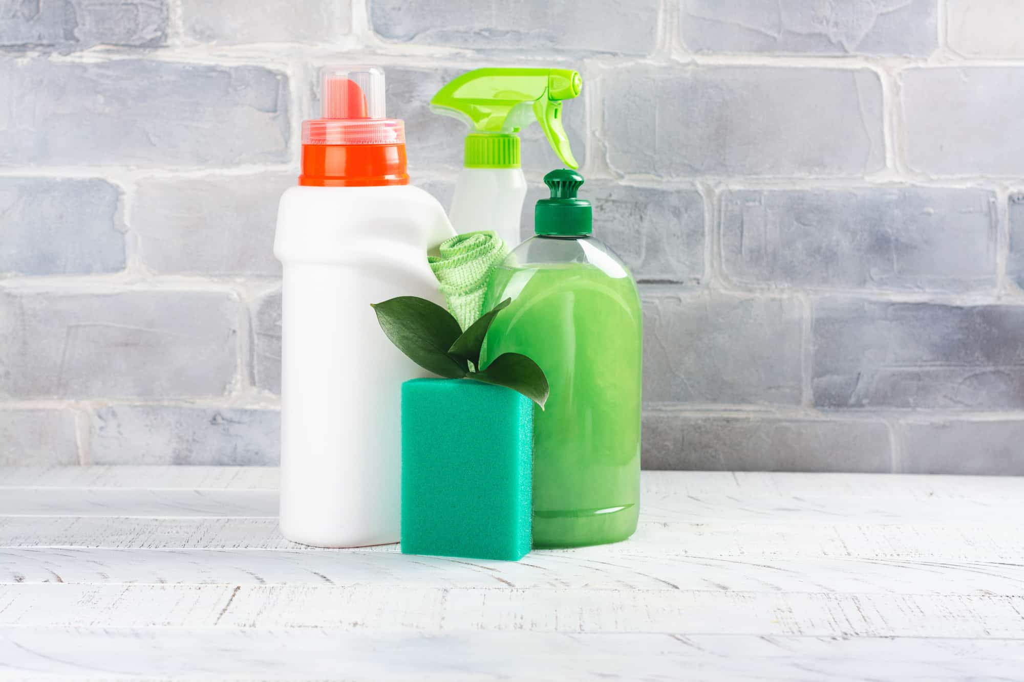 White and green bottles of cleaning solutions in front of a grey stone wall.