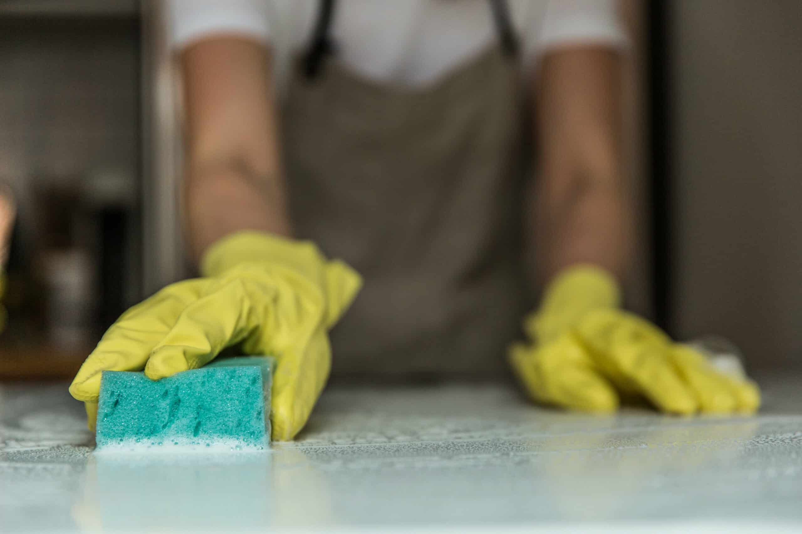 Maid in apron and yellow gloves cleaning counter.