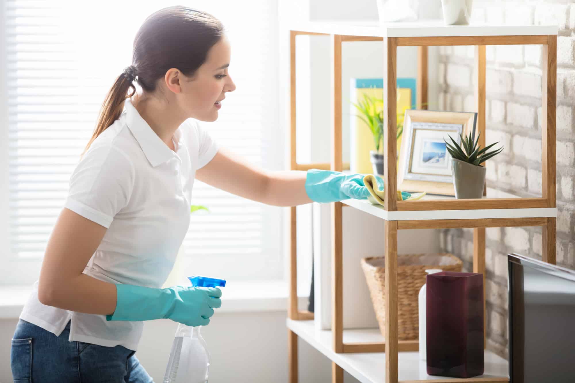 Woman cleaning wooden shelves In living room.