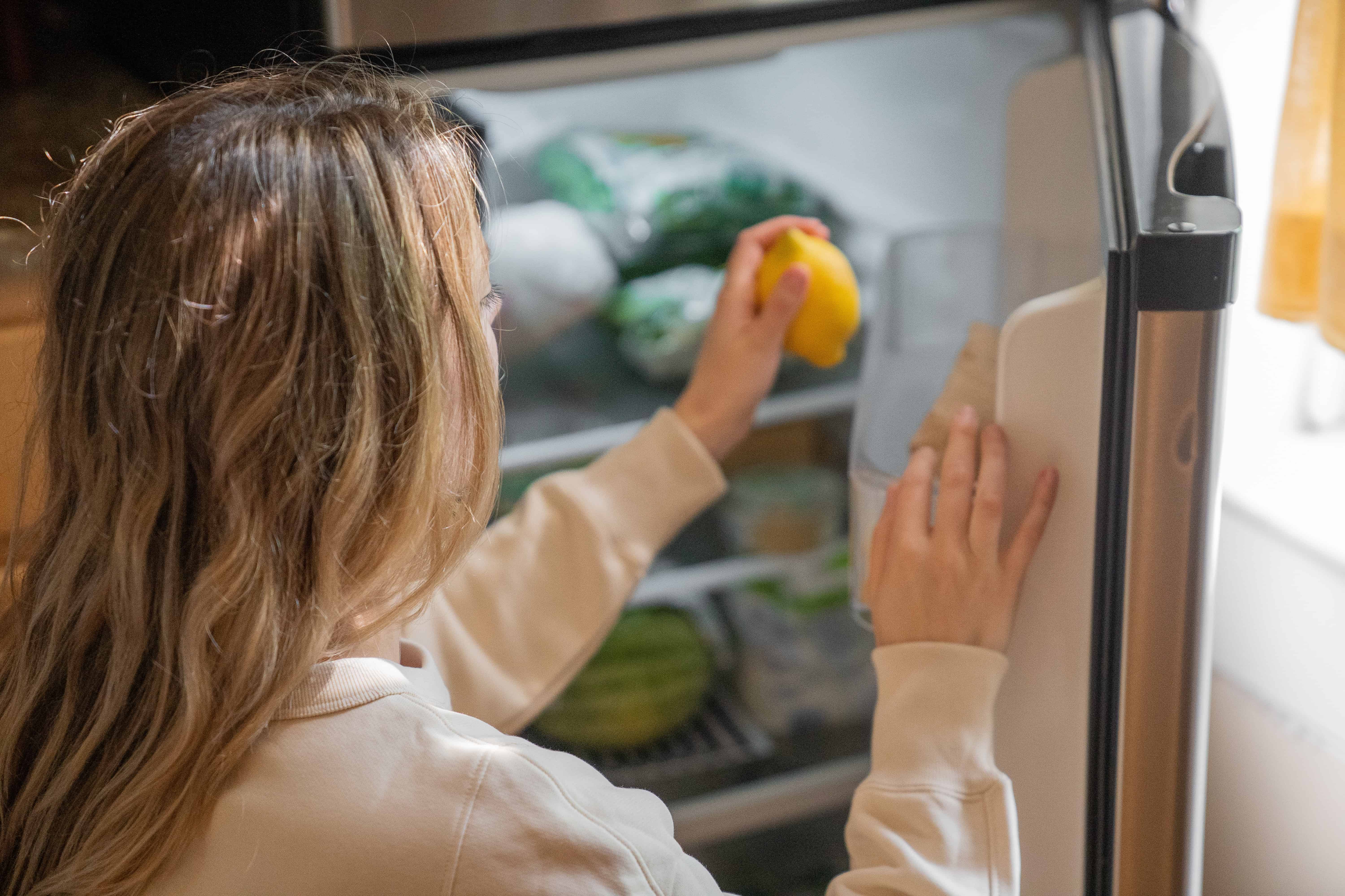 Woman taking lemon from refrigerator.