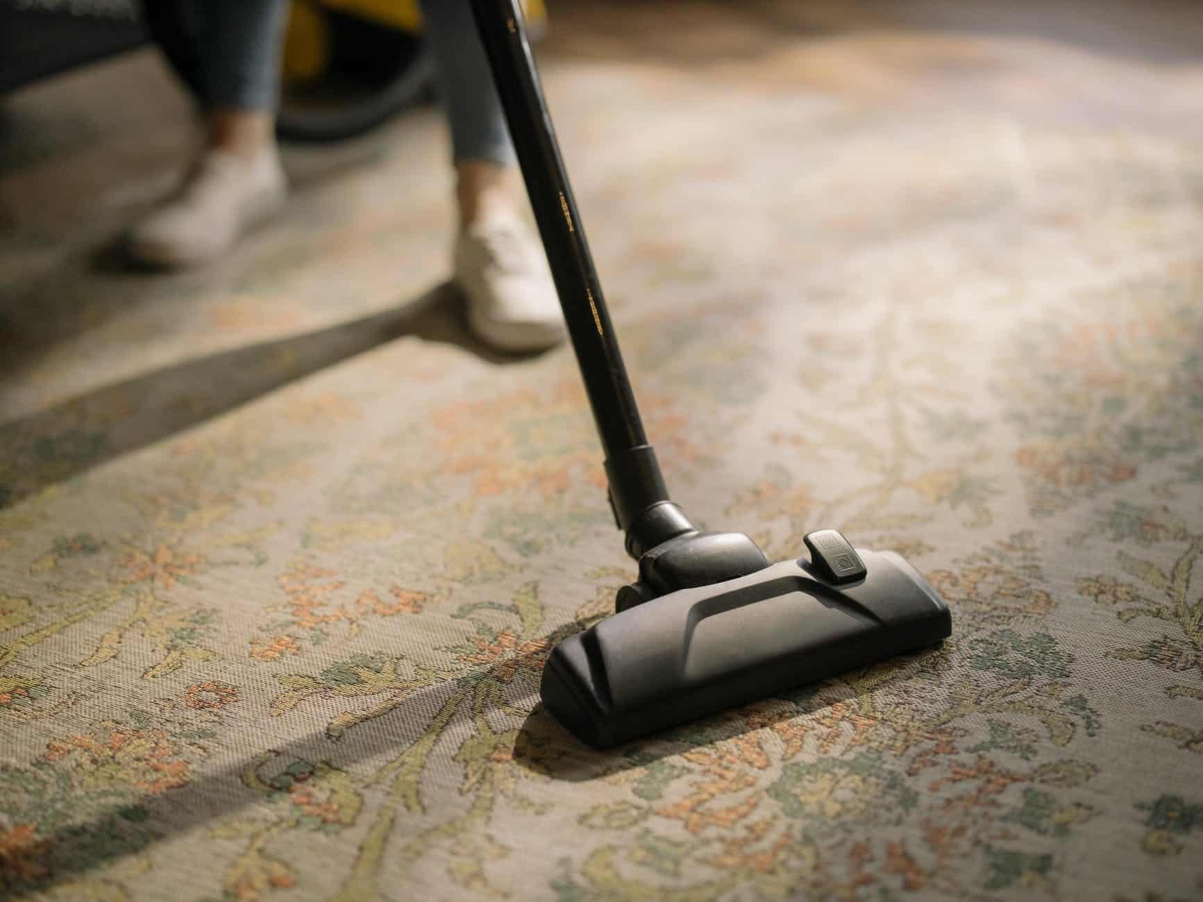 A person uses a vacuum cleaner on a rug.