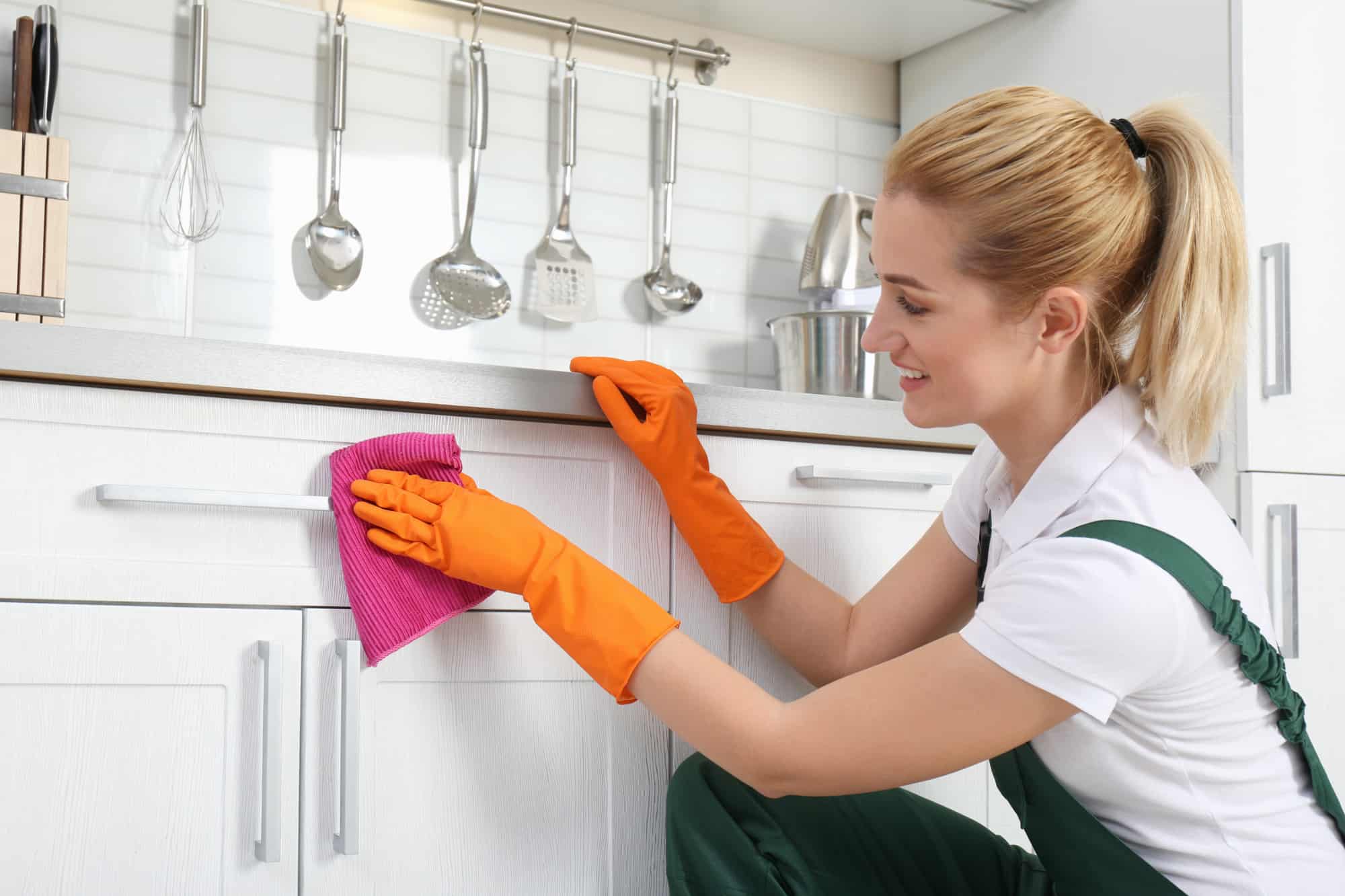 Woman wiping down kitchen cabinets with a cleaning cloth.