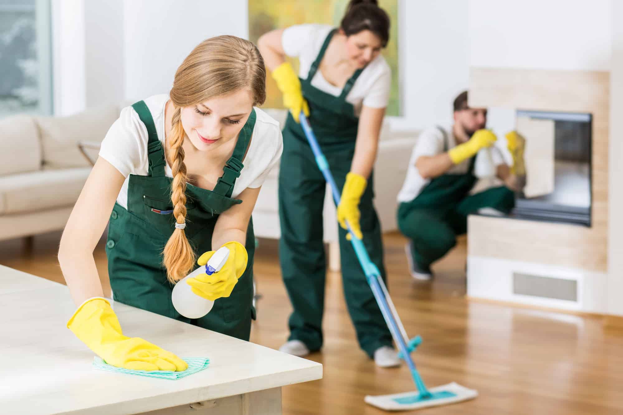 Cleaning lady wiping a countertop while two other cleaners working in the background.